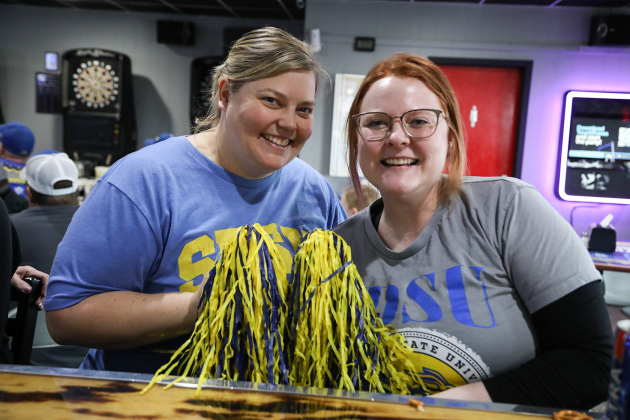 With pom poms at the ready, Pin Twisters owner Betsy Schroeder (left) and Kaci Anson cheer on the Jacks.